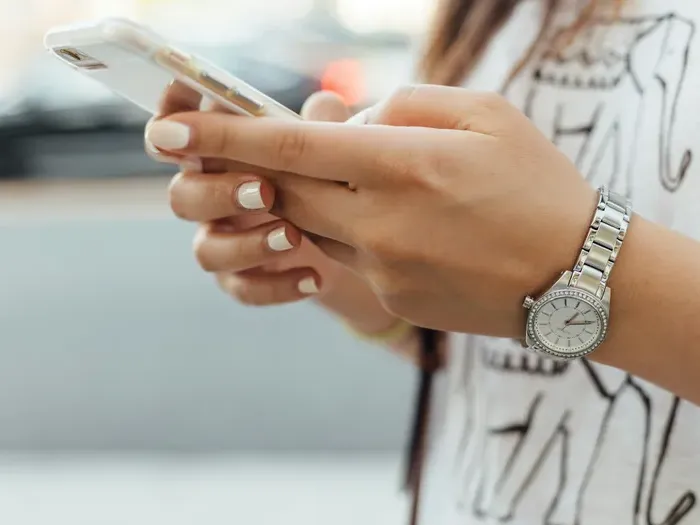 Close-up of woman’s hands holding smartphone while texting outdoors, wearing silver watch and casual shirt
